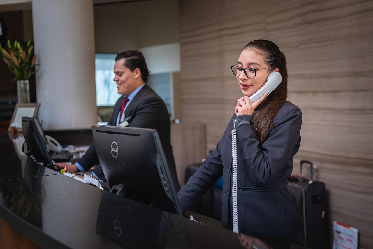 Two friendly reception staff behind the front desk of a resort, one on the phone and one greeting guests